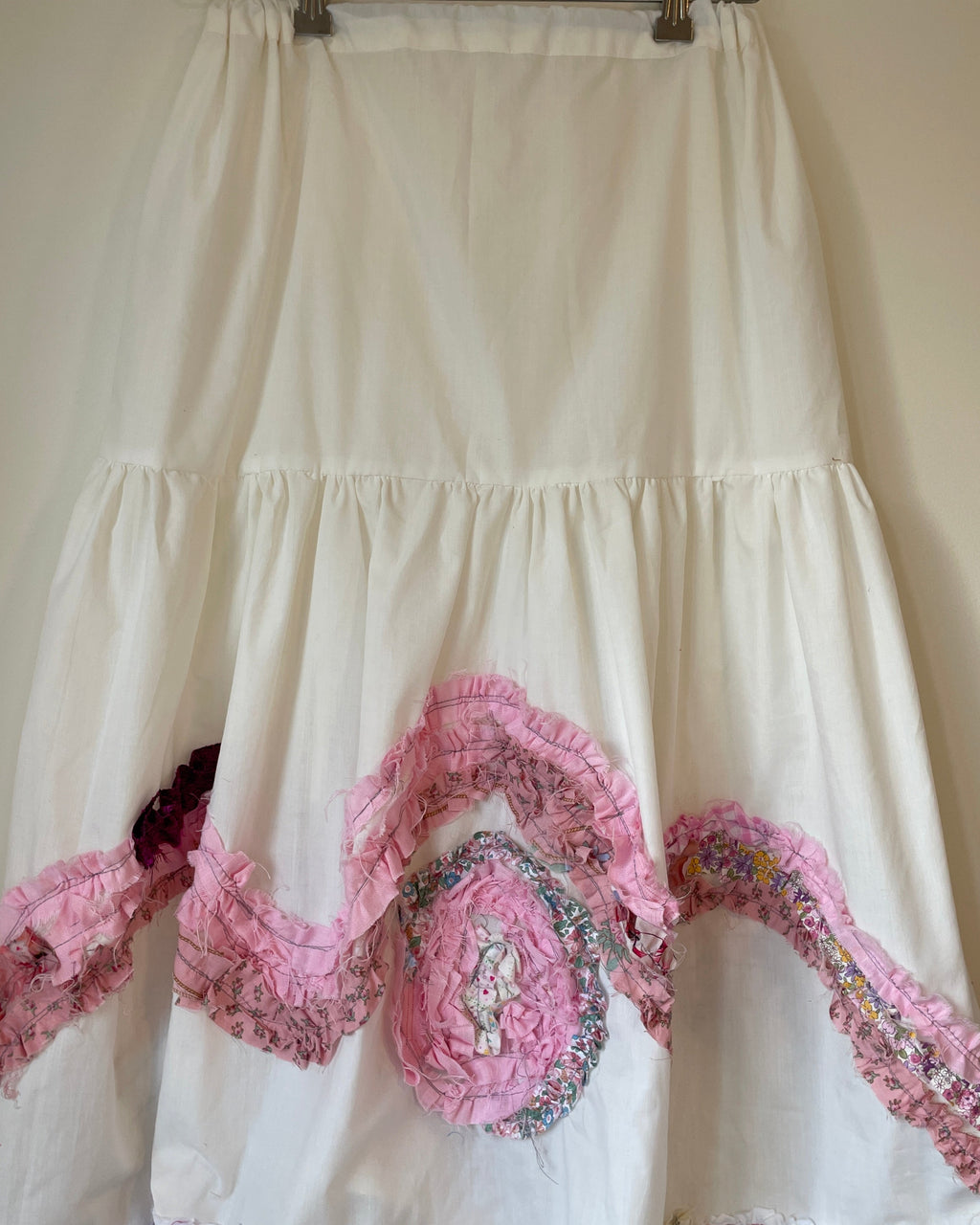 White dress with pink floral embellishments on a hanger against a plain background