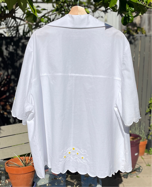 White blouse with lace details on a mannequin against a garden background