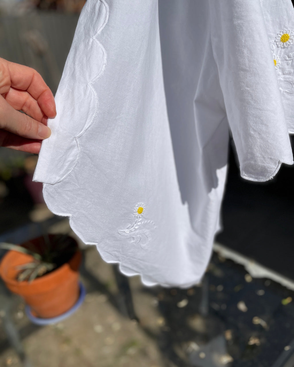 White blouse with floral embroidery held by a hand, blurred background