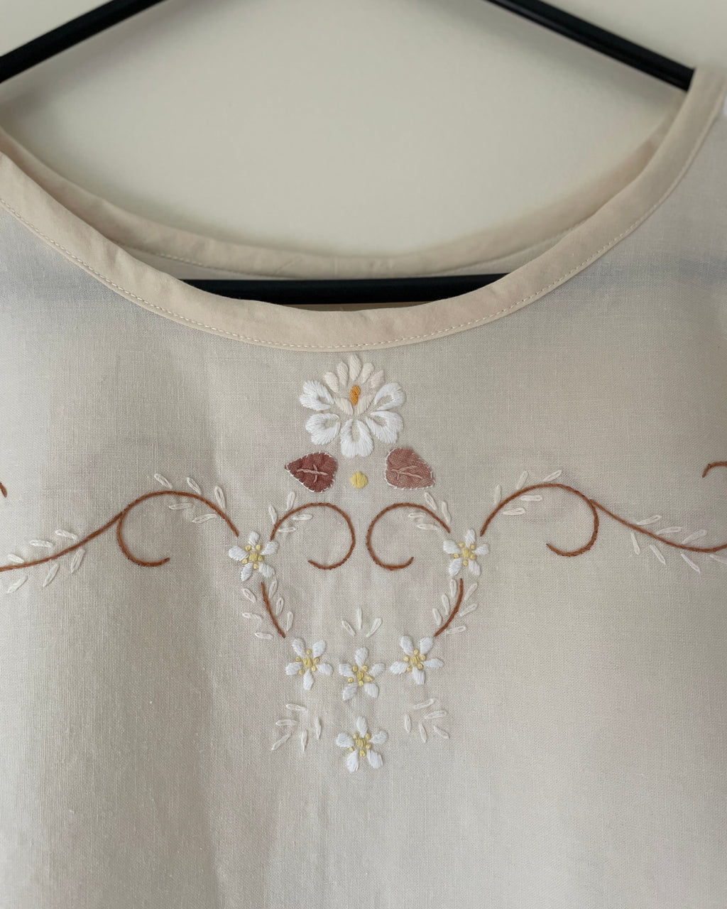 Embroidered floral design on a beige fabric with a hanger in the background.