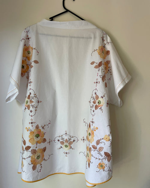 White blouse with floral patterns on a hanger against a beige wall