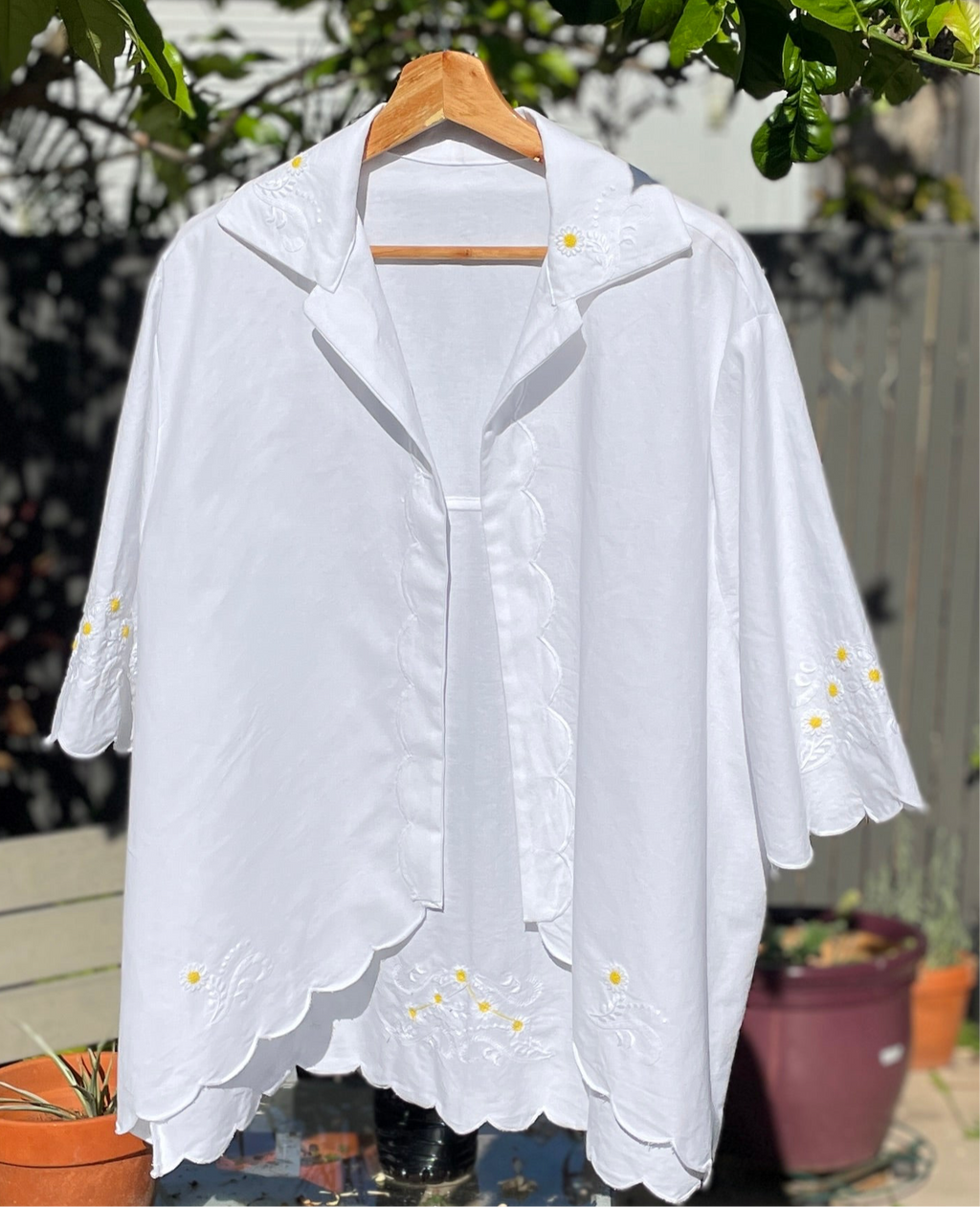 White blouse with floral embroidery on a wooden hanger against a natural background