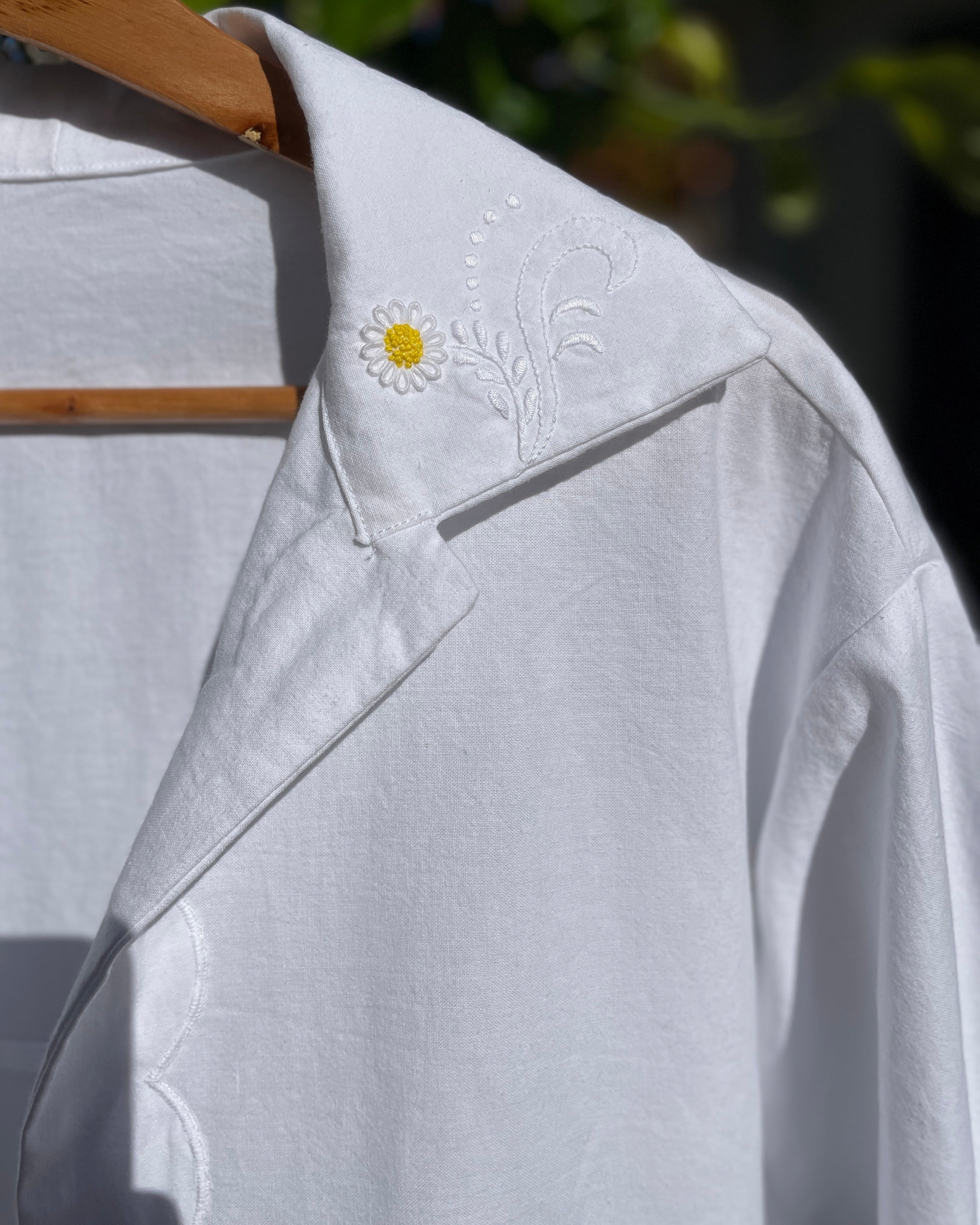 White shirt with a daisy flower embroidery on a wooden hanger against a blurred natural background