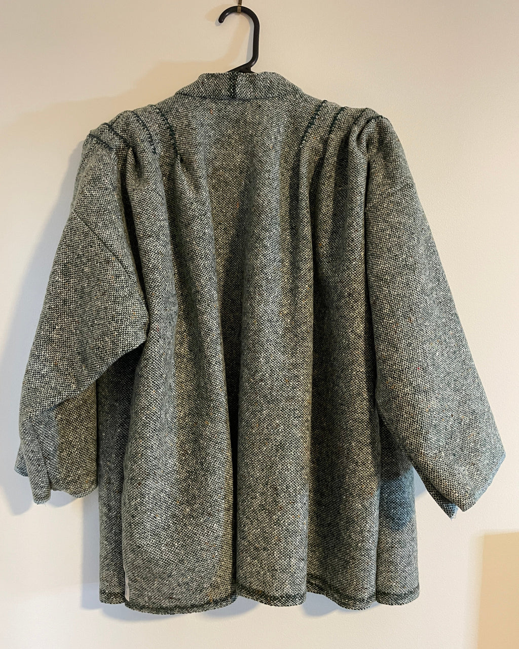 Gray and green textured coat on a hanger against a white wall