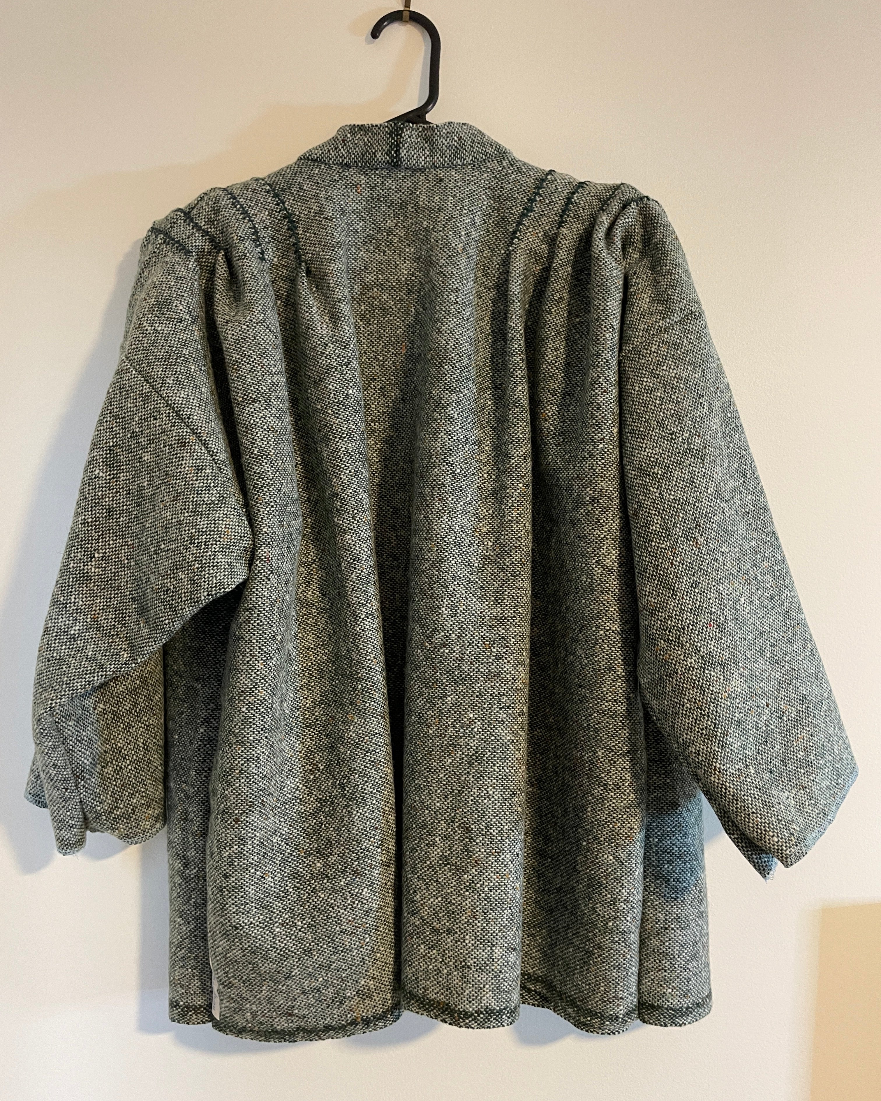 Gray and green textured coat on a hanger against a white wall