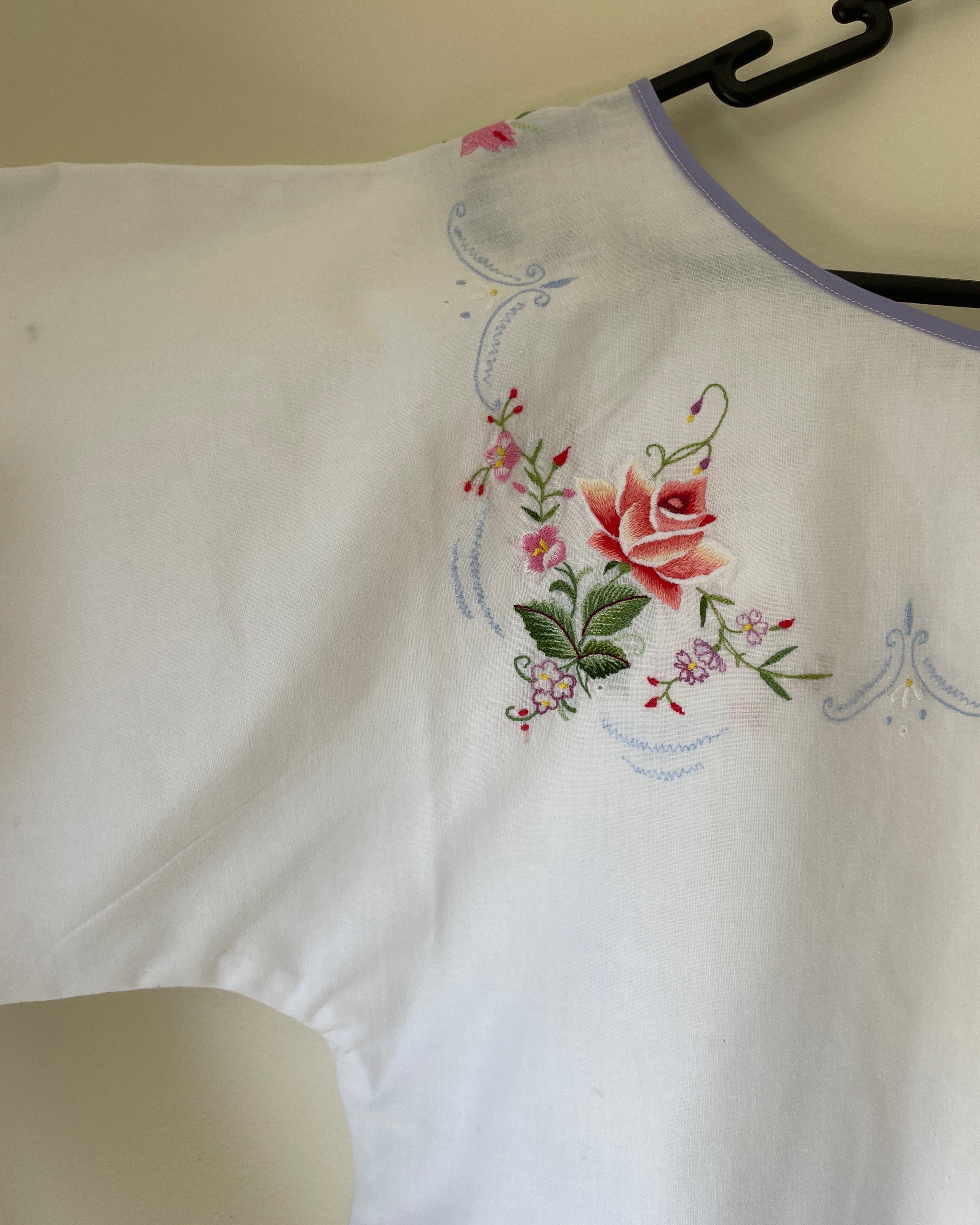 Embroidered floral design on a white fabric with a hanger in the background