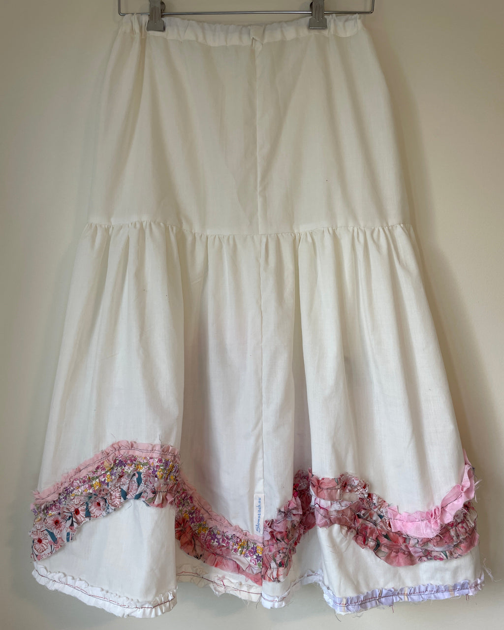 White dress with floral trim on a hanger against a plain background