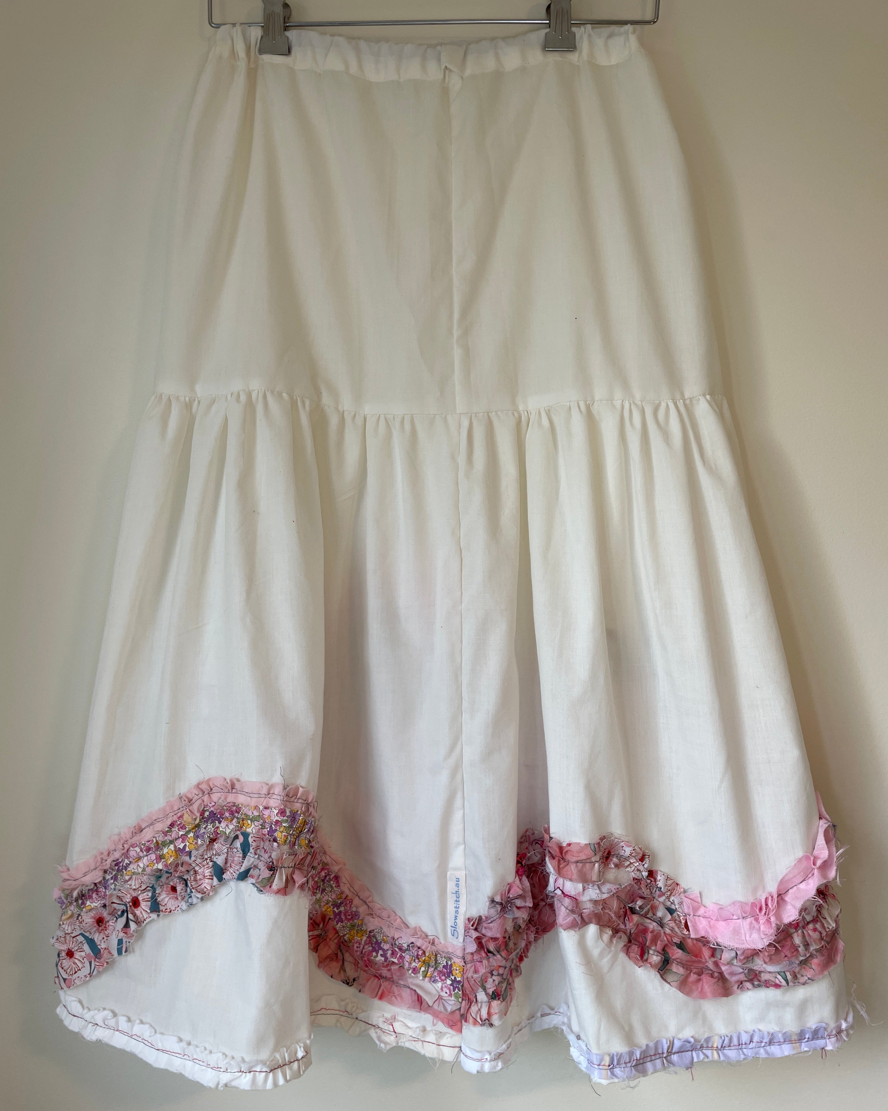 White dress with floral trim on a hanger against a plain background