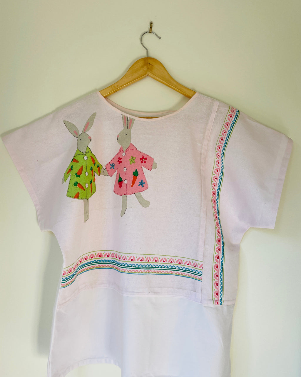 White blouse with bunnies on a wooden hanger against a white wall