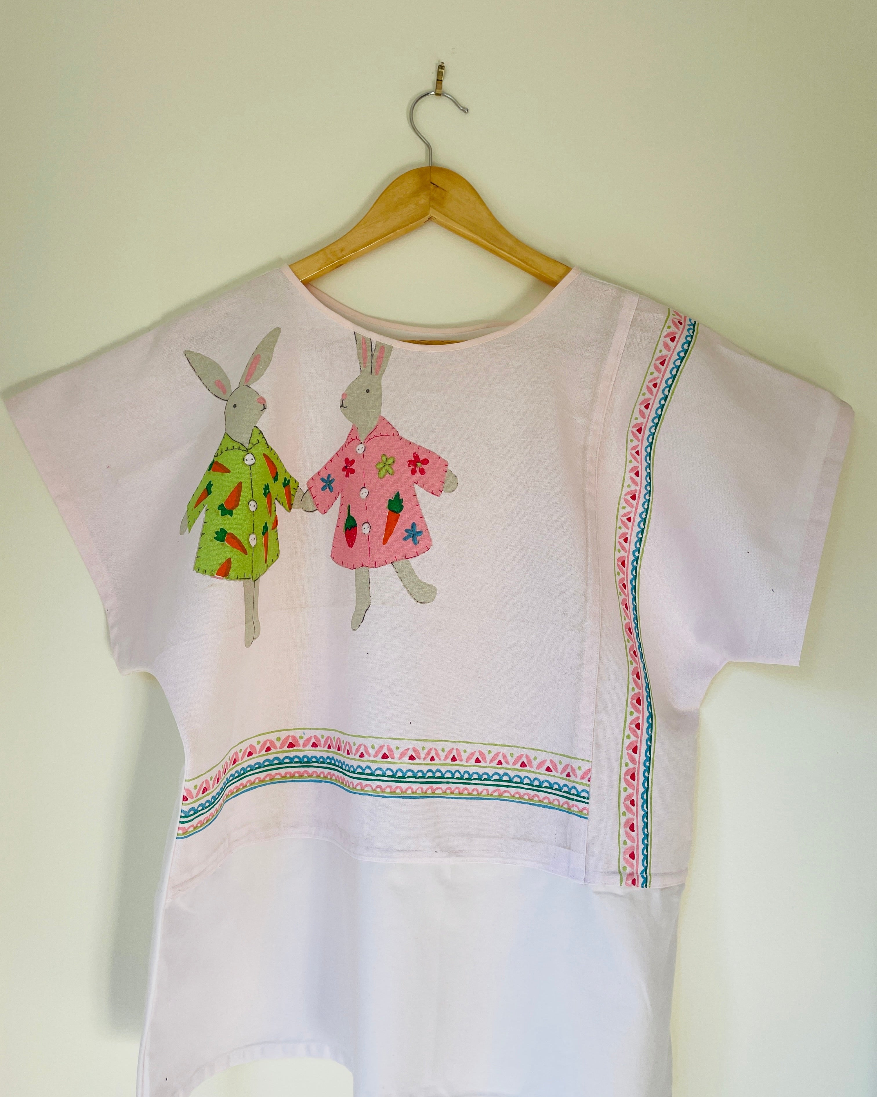 White blouse with bunnies on a wooden hanger against a white wall