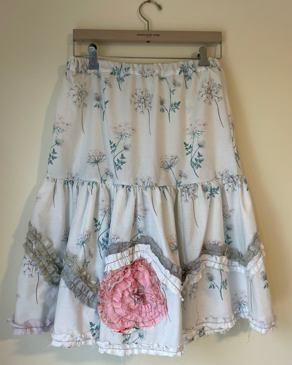 Floral dress with a large pink flower on a hanger against a beige wall.