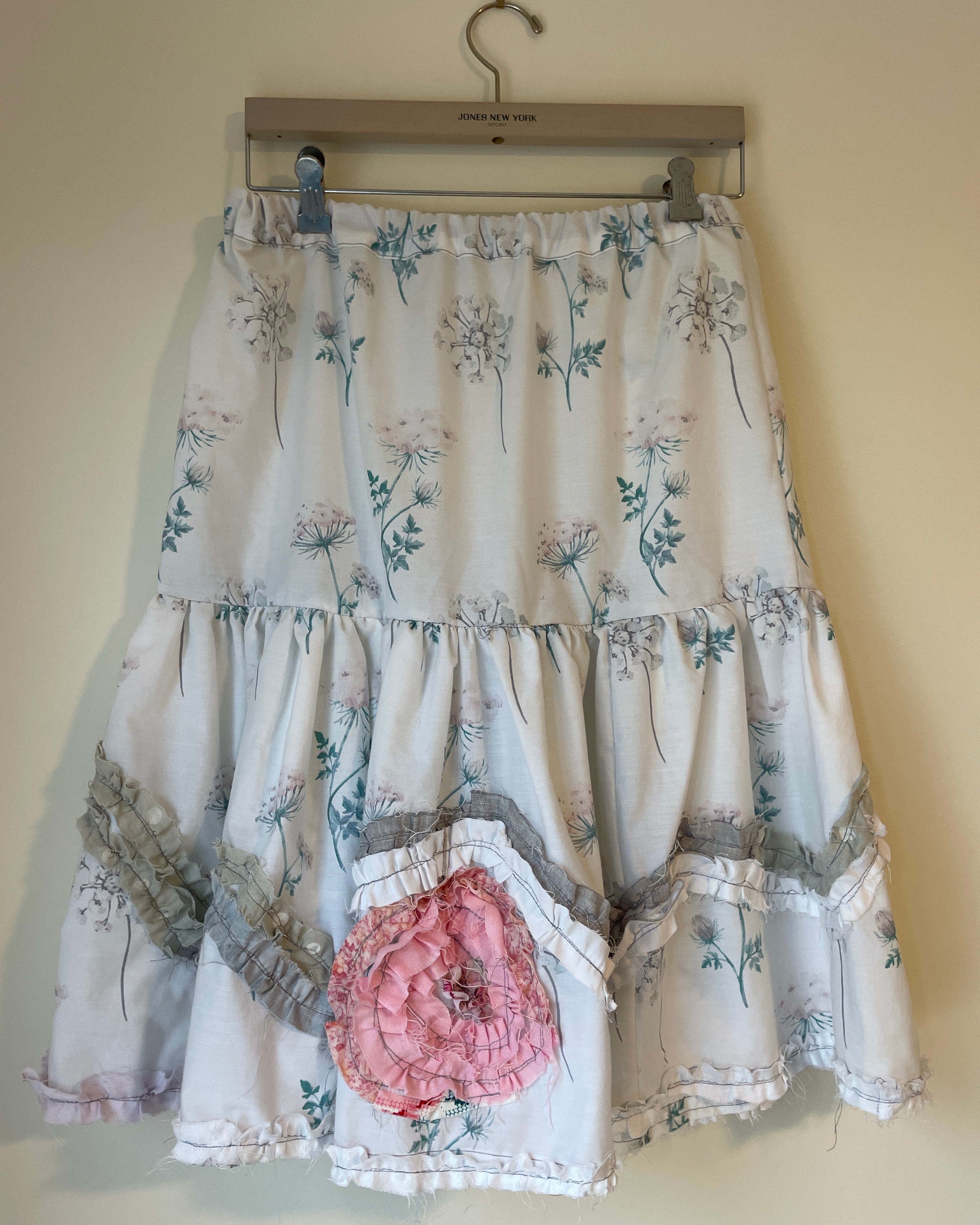 Floral dress with a large pink flower on a hanger against a beige wall.