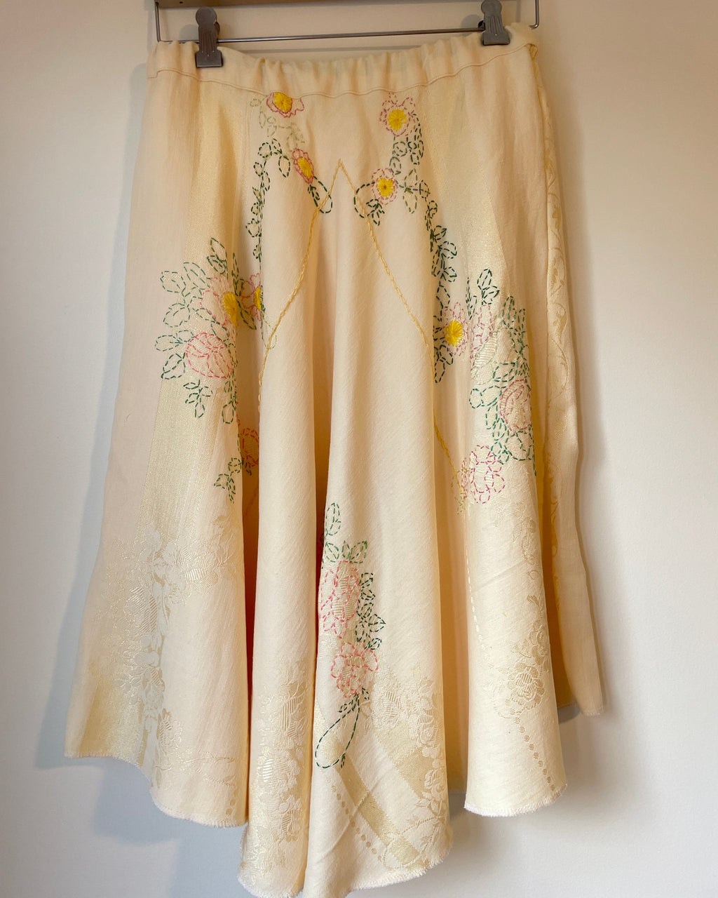 Yellow embroidered skirt hanging on a rack against a plain wall.