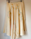 Yellow embroidered skirt hanging on a rack against a plain wall.