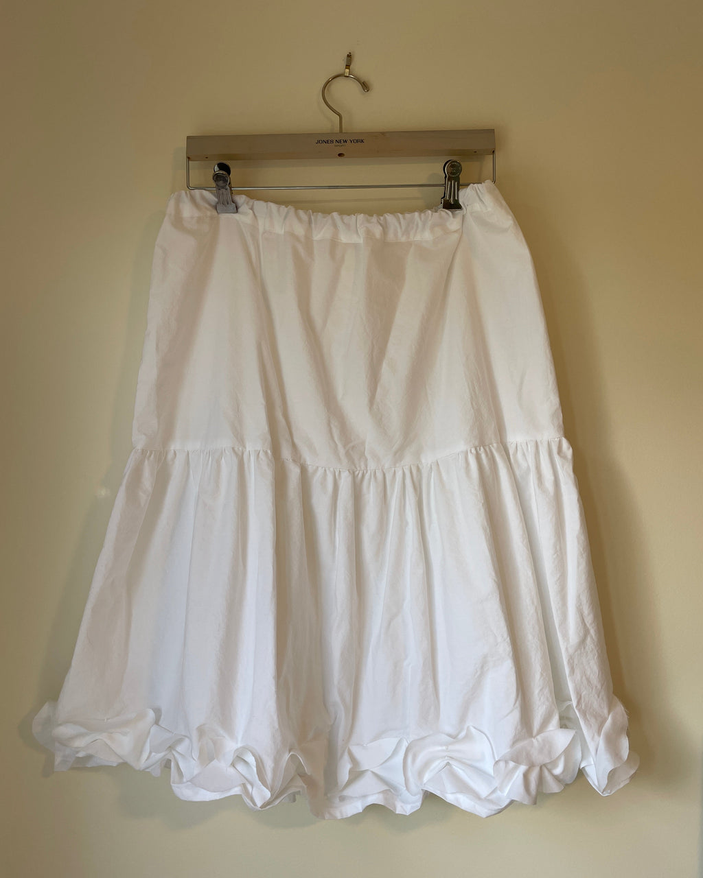 White skirt on a wooden hanger against a beige wall