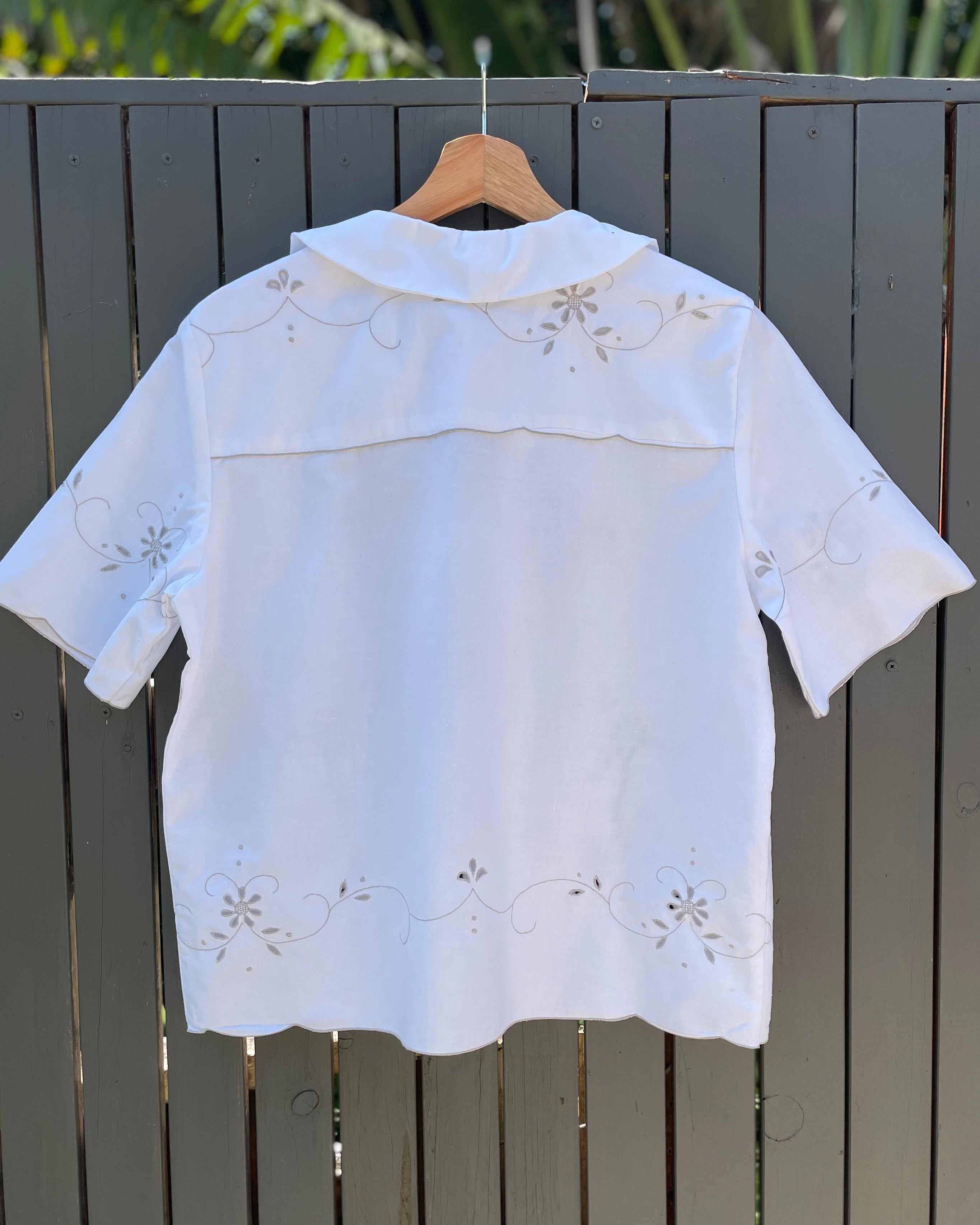 White embroidered blouse on a hanger against a wooden fence background
