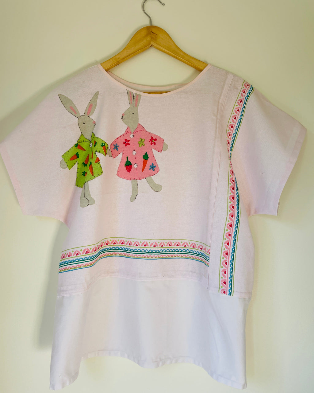 White blouse with bunnies on a wooden hanger against a light background