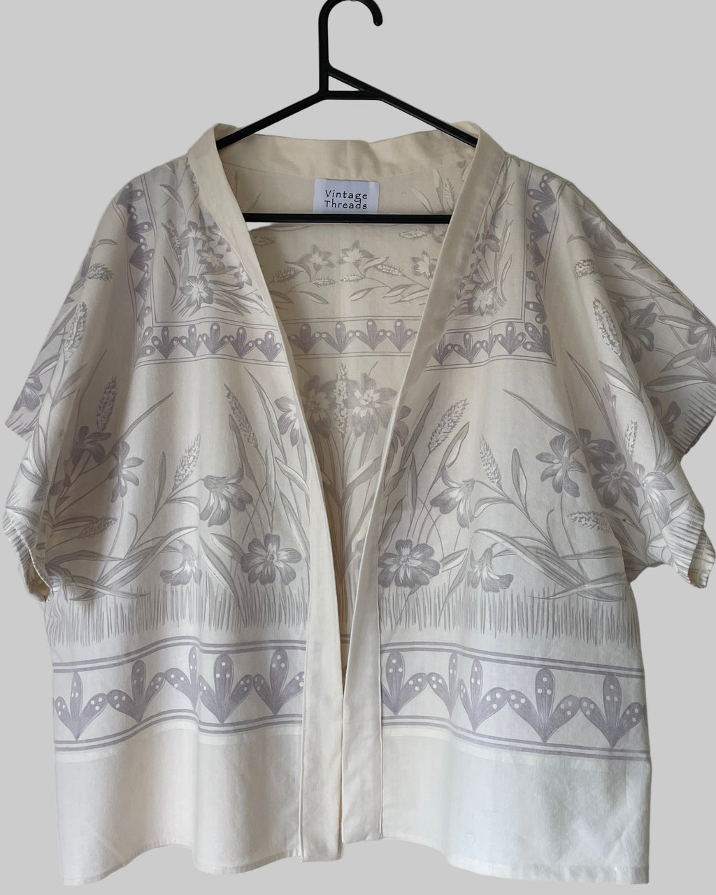 White kimono-style garment with gray floral patterns on a hanger against a white background