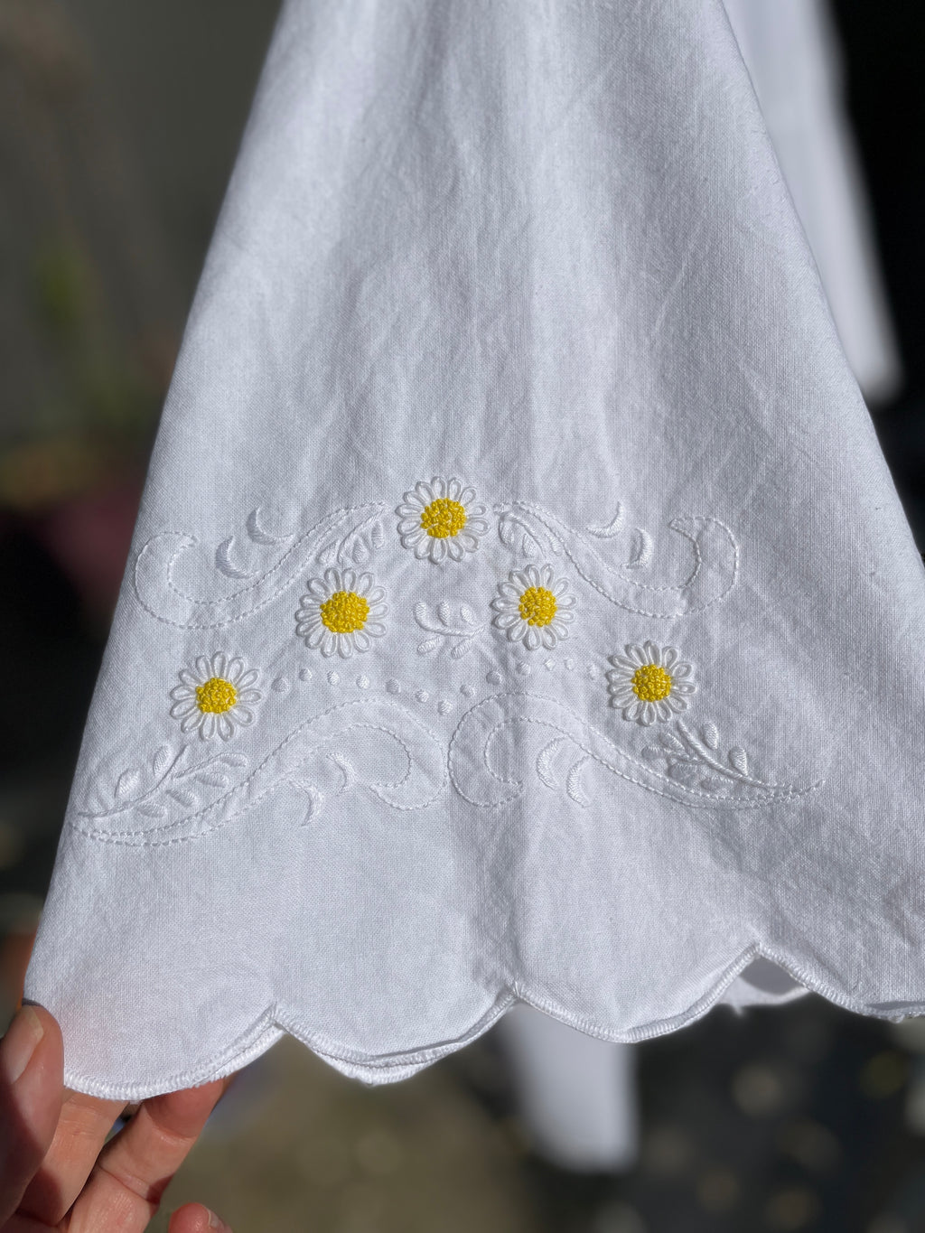 White fabric with embroidered daisy flowers held by a hand against a blurred background