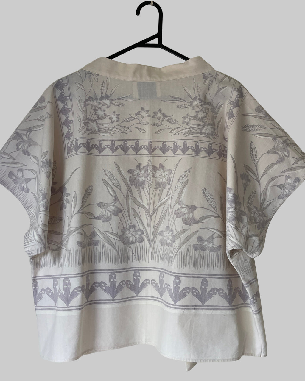 Cream blouse with floral pattern on a hanger against a white background