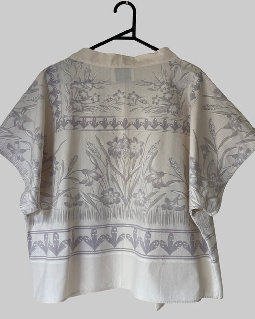 Cream blouse with floral pattern on a hanger against a white background