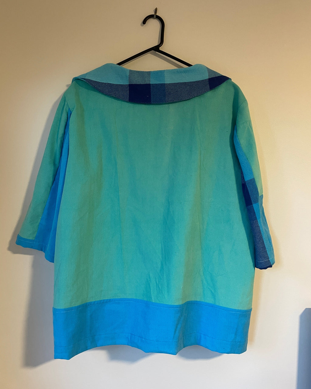 Green and blue jacket on a hanger against a beige wall