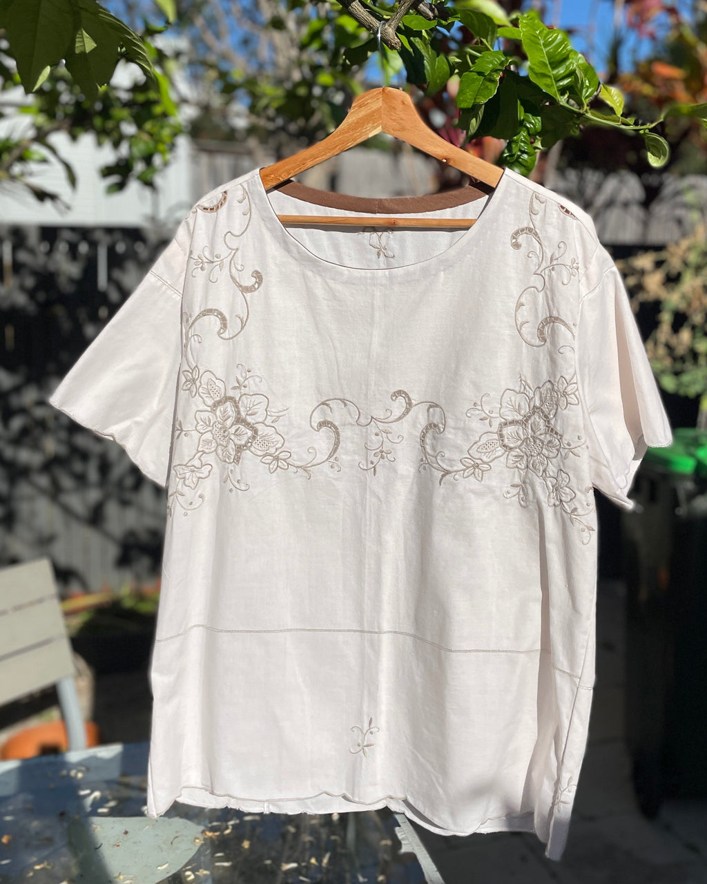 White embroidered blouse on a hanger outdoors with trees and a house in the background