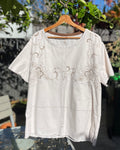 White embroidered blouse on a hanger outdoors with trees and a house in the background