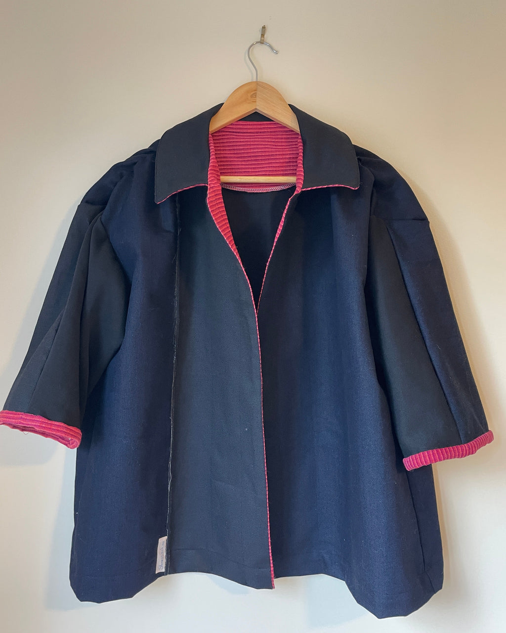 Navy jacket with pink trim on a wooden hanger against a white wall