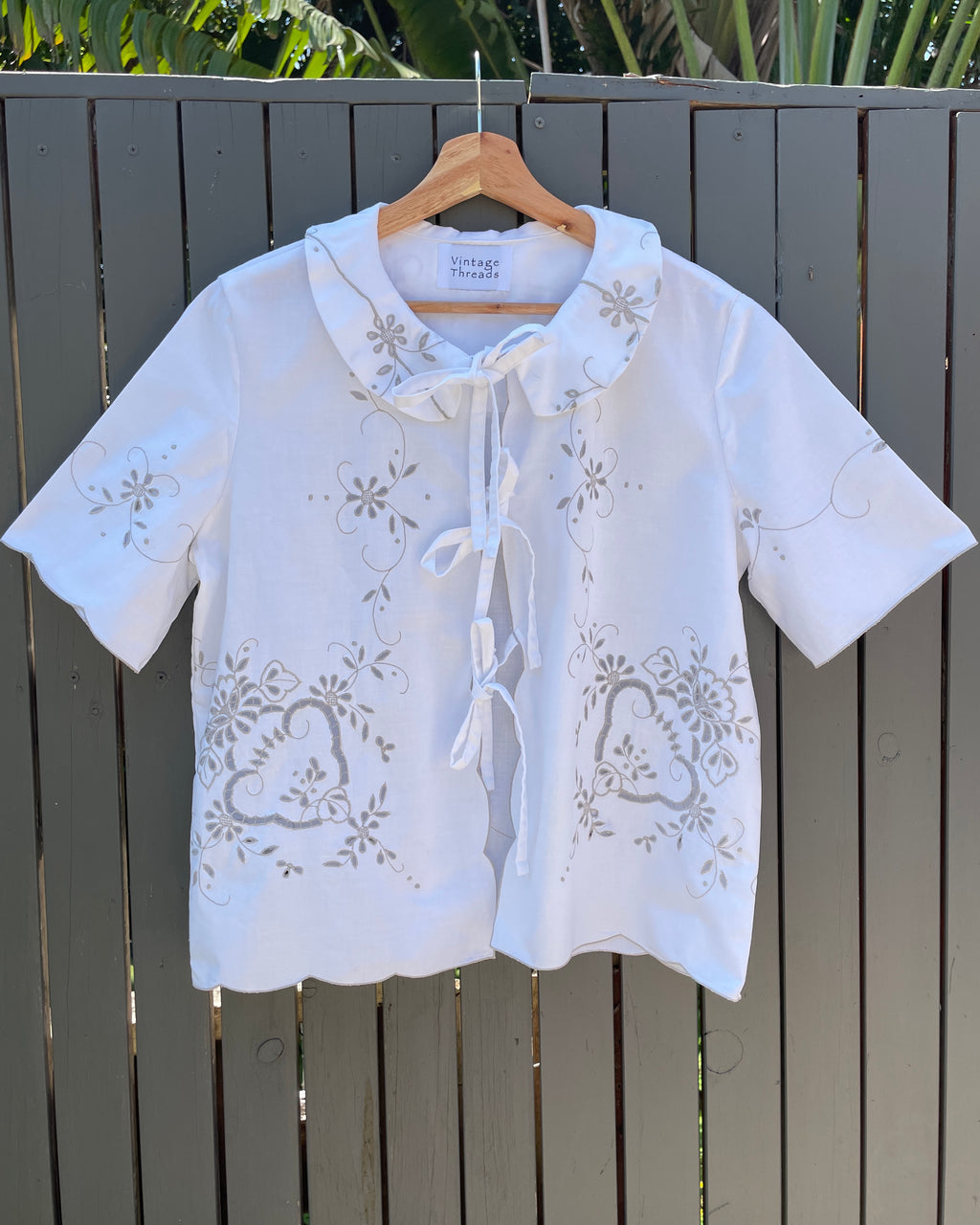 White embroidered blouse on a wooden hanger against a wooden fence background