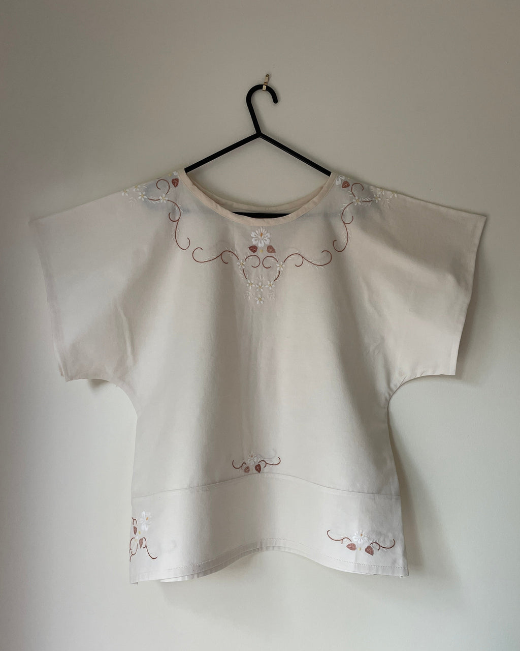 White blouse with embroidery on a hanger against a plain wall