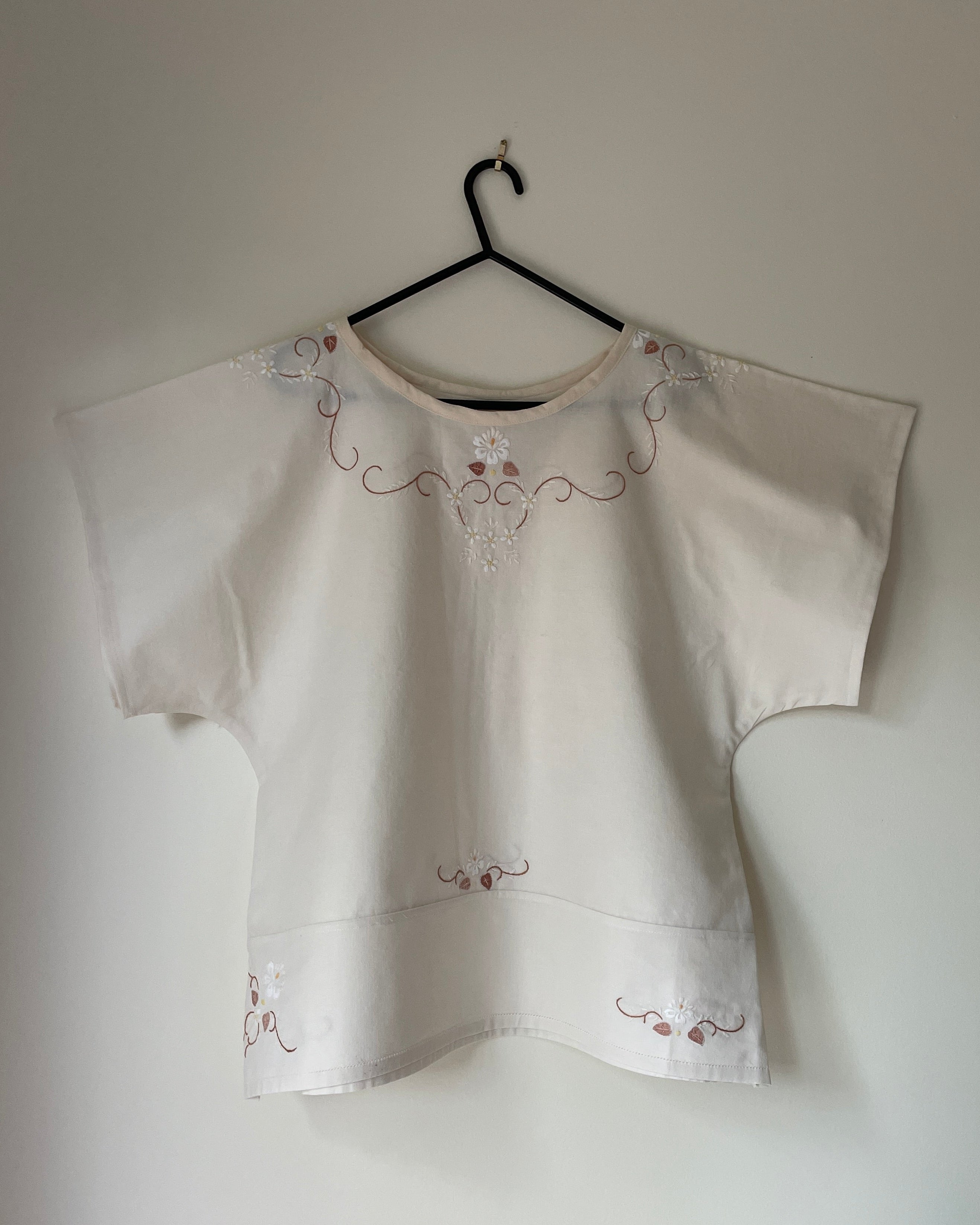 White blouse with embroidery on a hanger against a plain wall