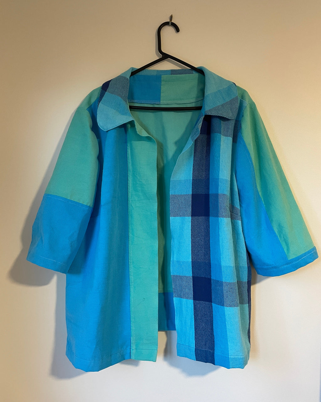 Blue and green plaid jacket on a hanger against a beige wall.