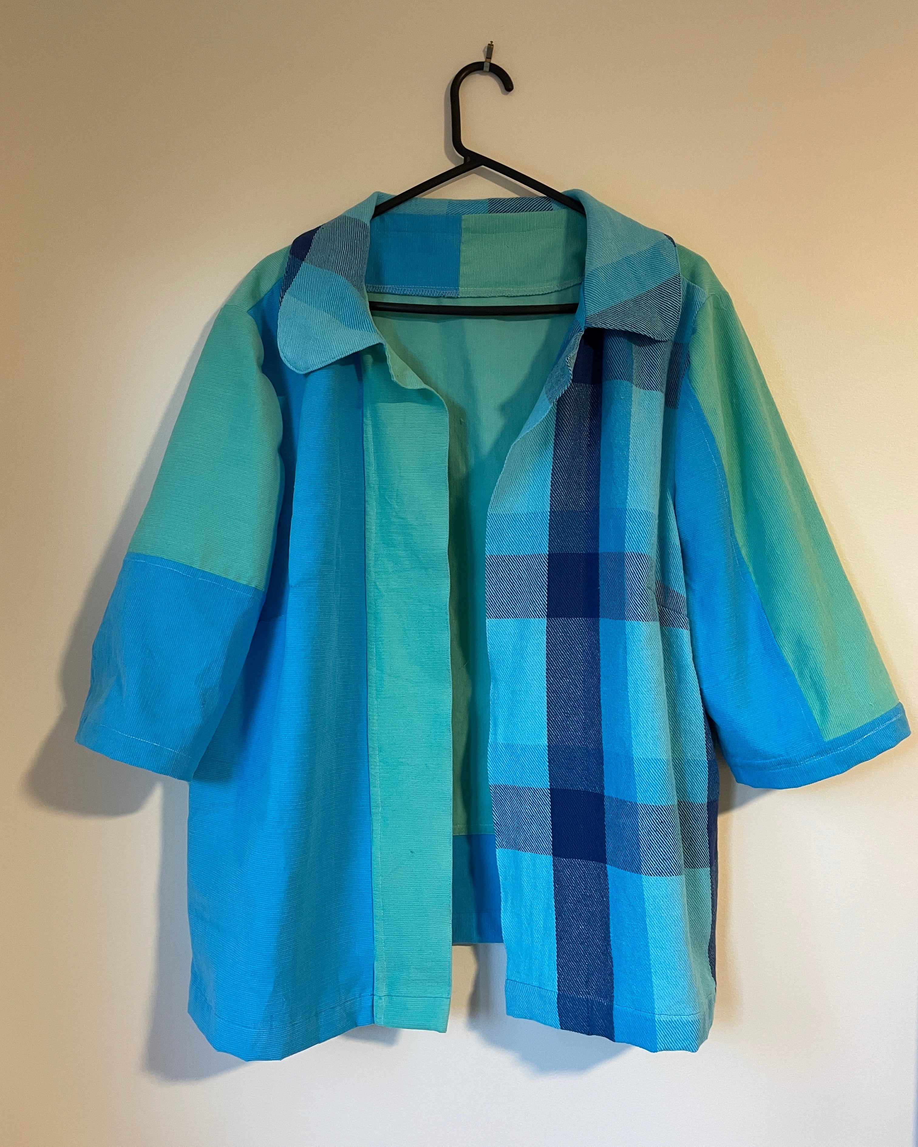 Blue and green plaid jacket on a hanger against a beige wall.