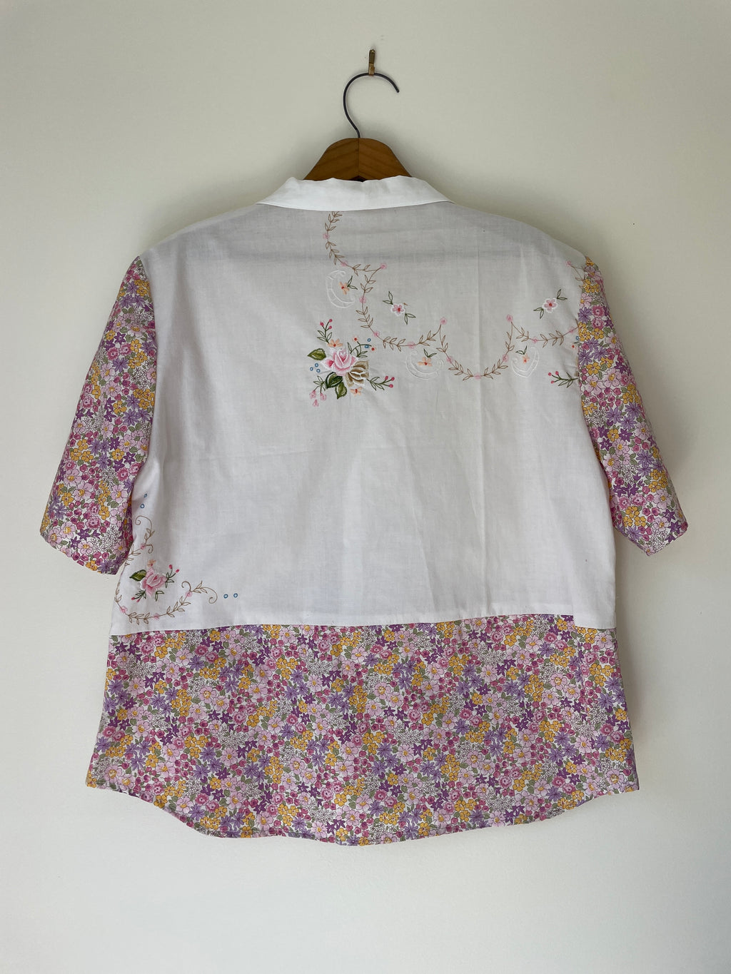 Floral-patterned blouse with embroidery on a wooden hanger against a white wall