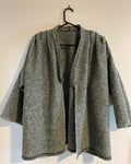 Gray and green textured coat on a hanger against a white wall