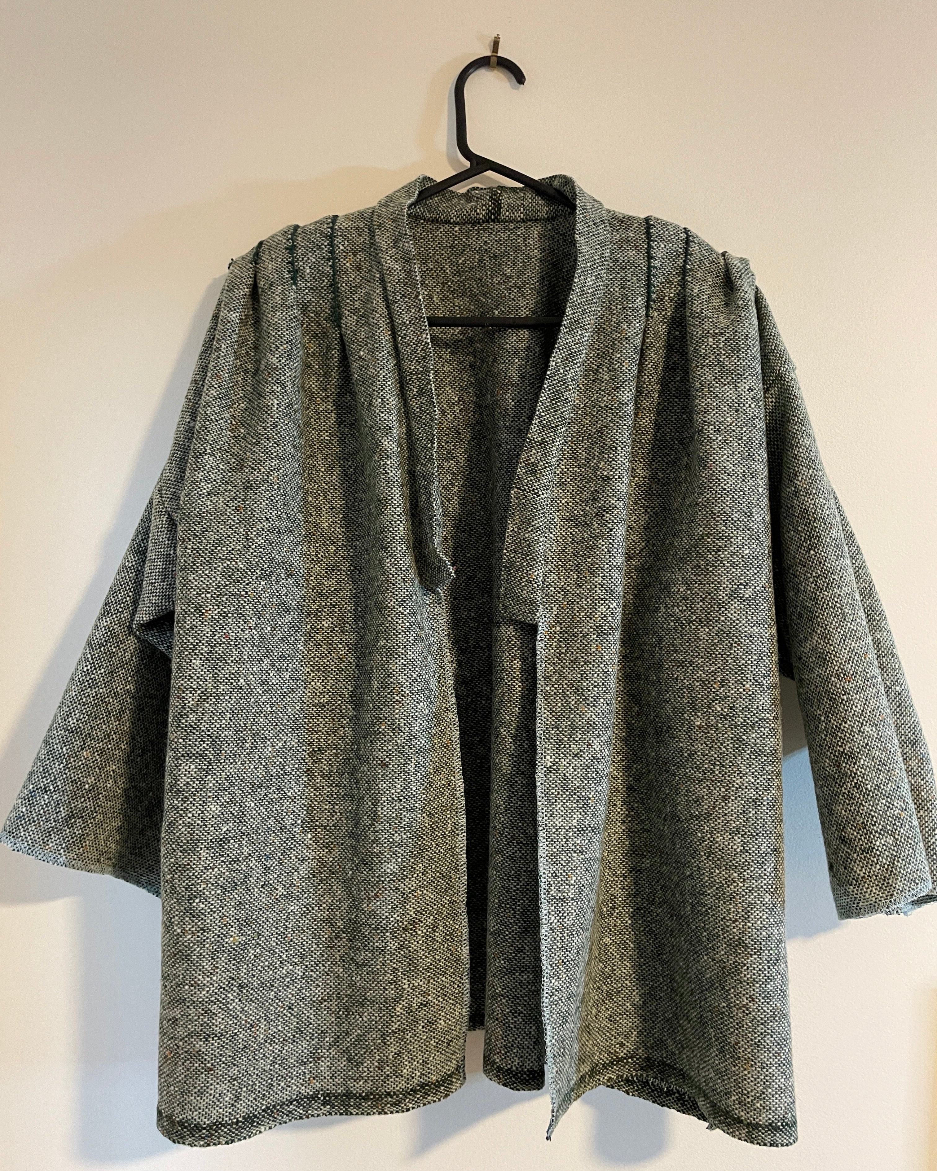 Gray and green textured coat on a hanger against a white wall