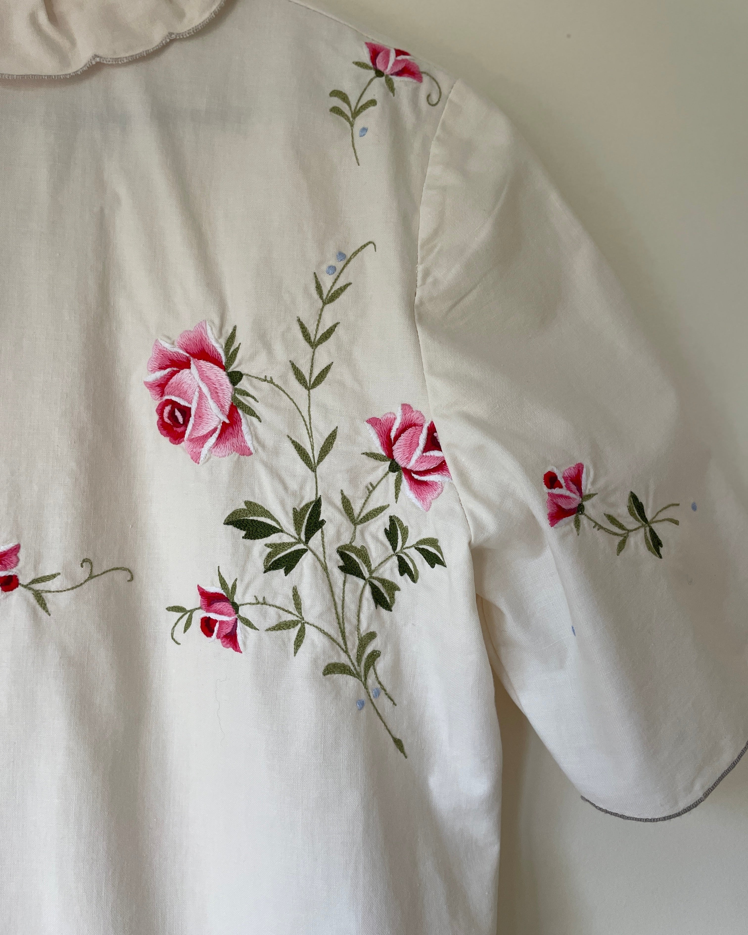 White garment with pink floral embroidery on a plain background