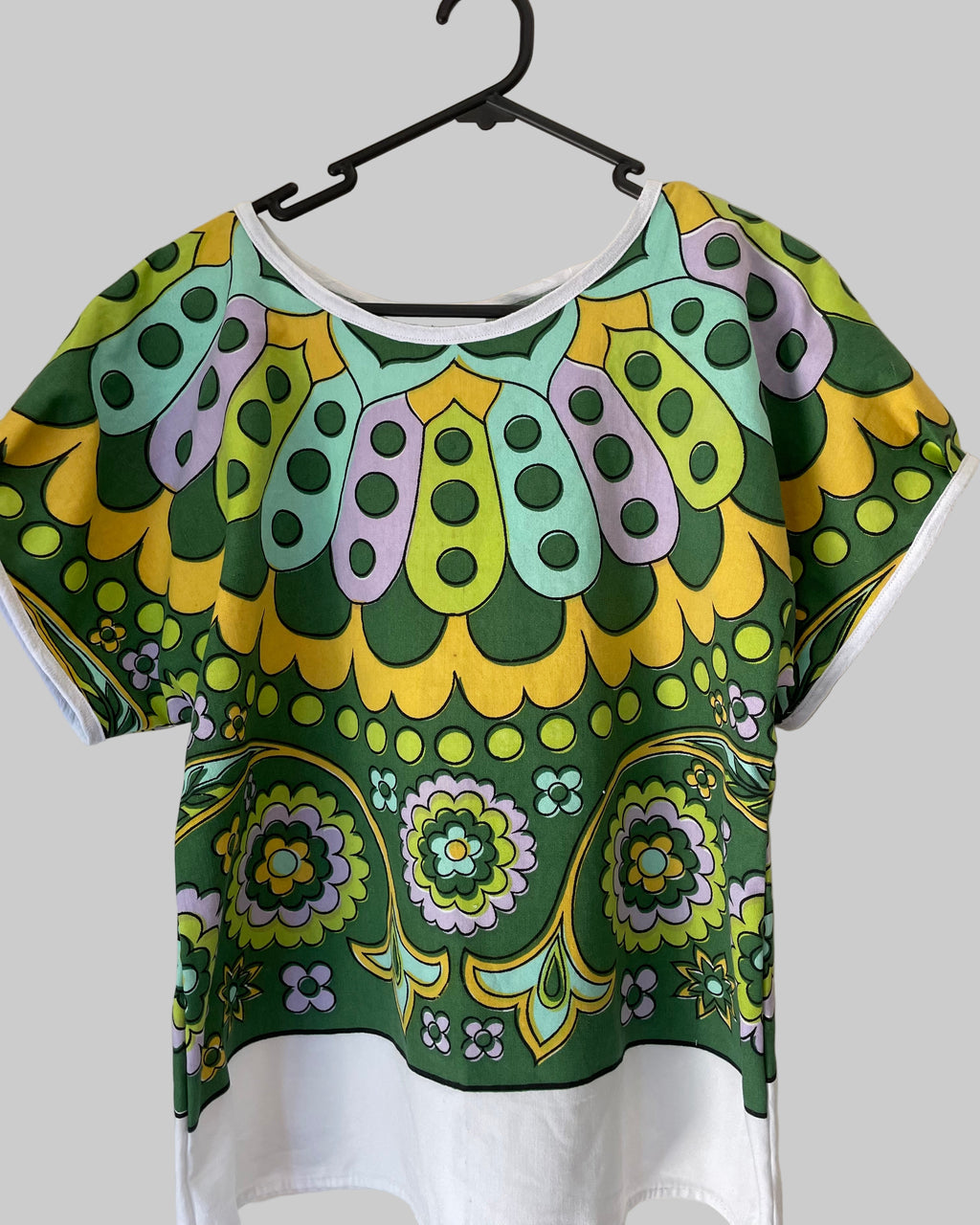 Colorful patterned top on a hanger against a plain background
