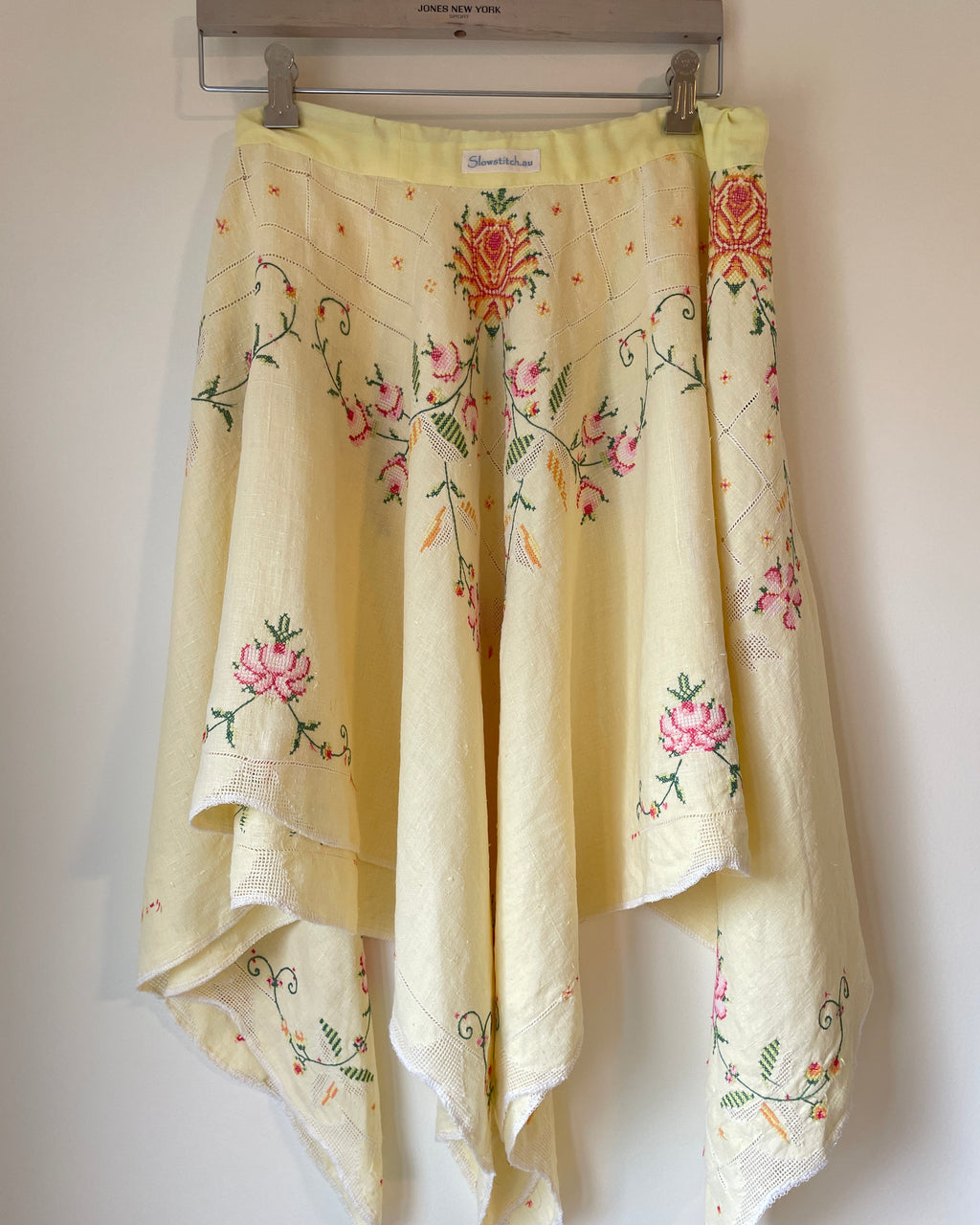 Embroidered floral skirt hanging on a rack against a white wall