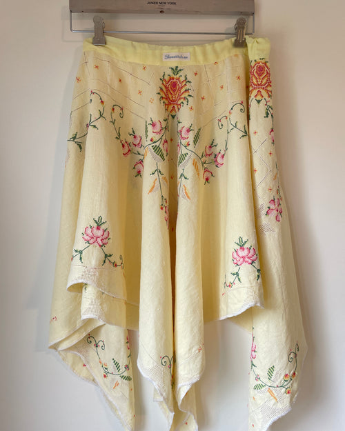 Embroidered floral skirt hanging on a rack against a white wall