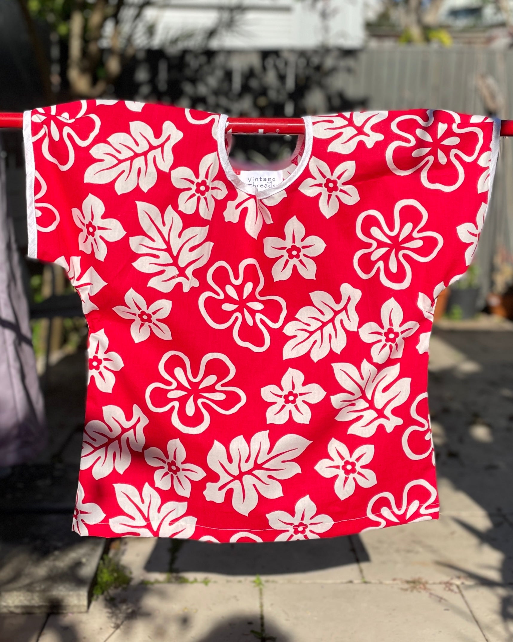 Red shirt with white floral pattern hanging on a clothesline outdoors.