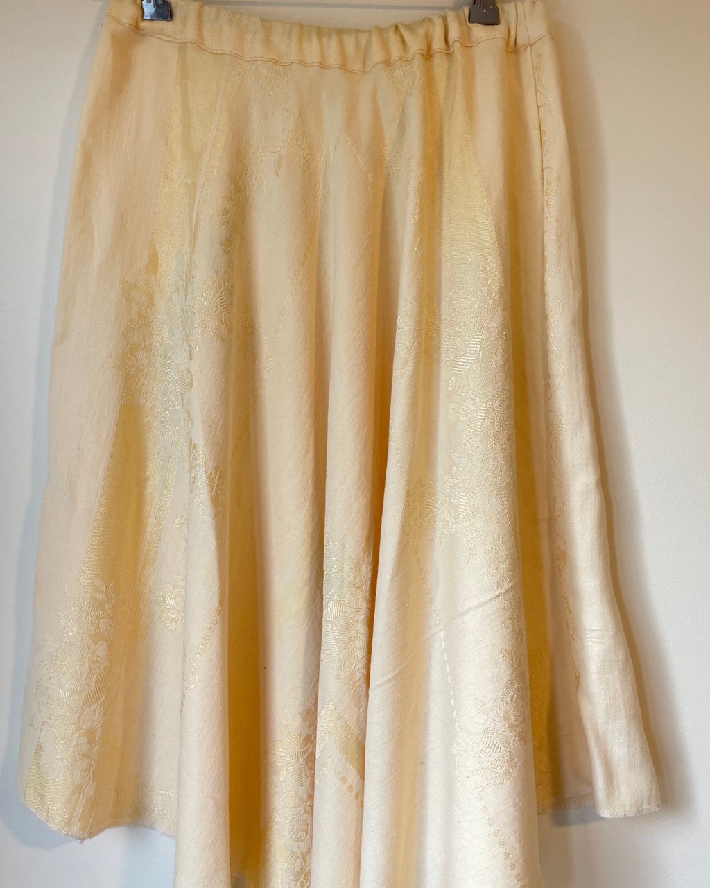 Folded yellow skirt on a metal hanger against a white background