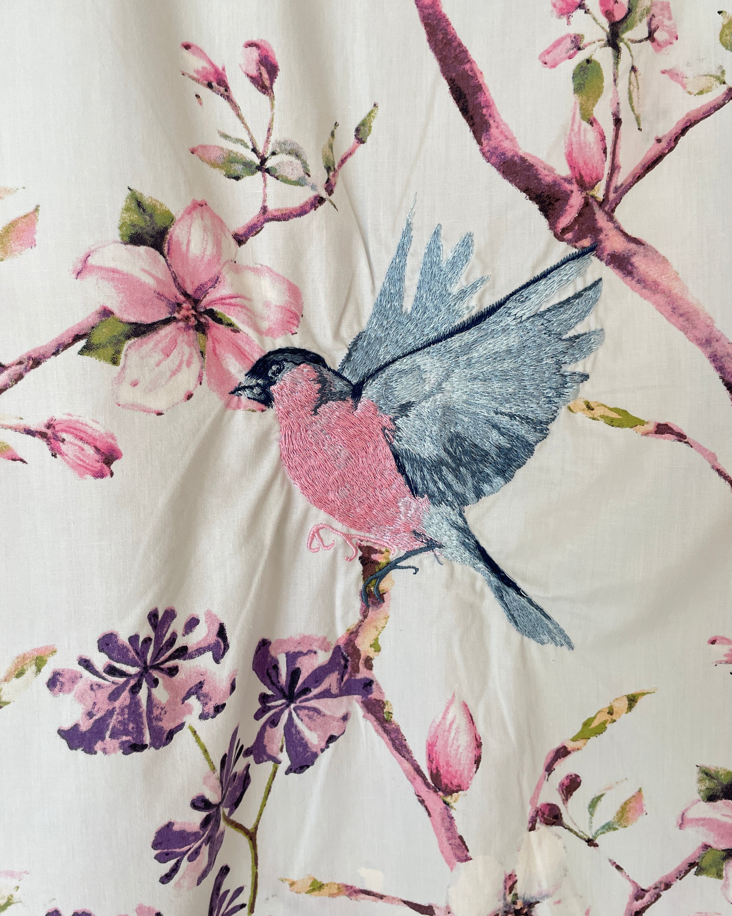 Embroidered fabric with a bird and floral design on a white background