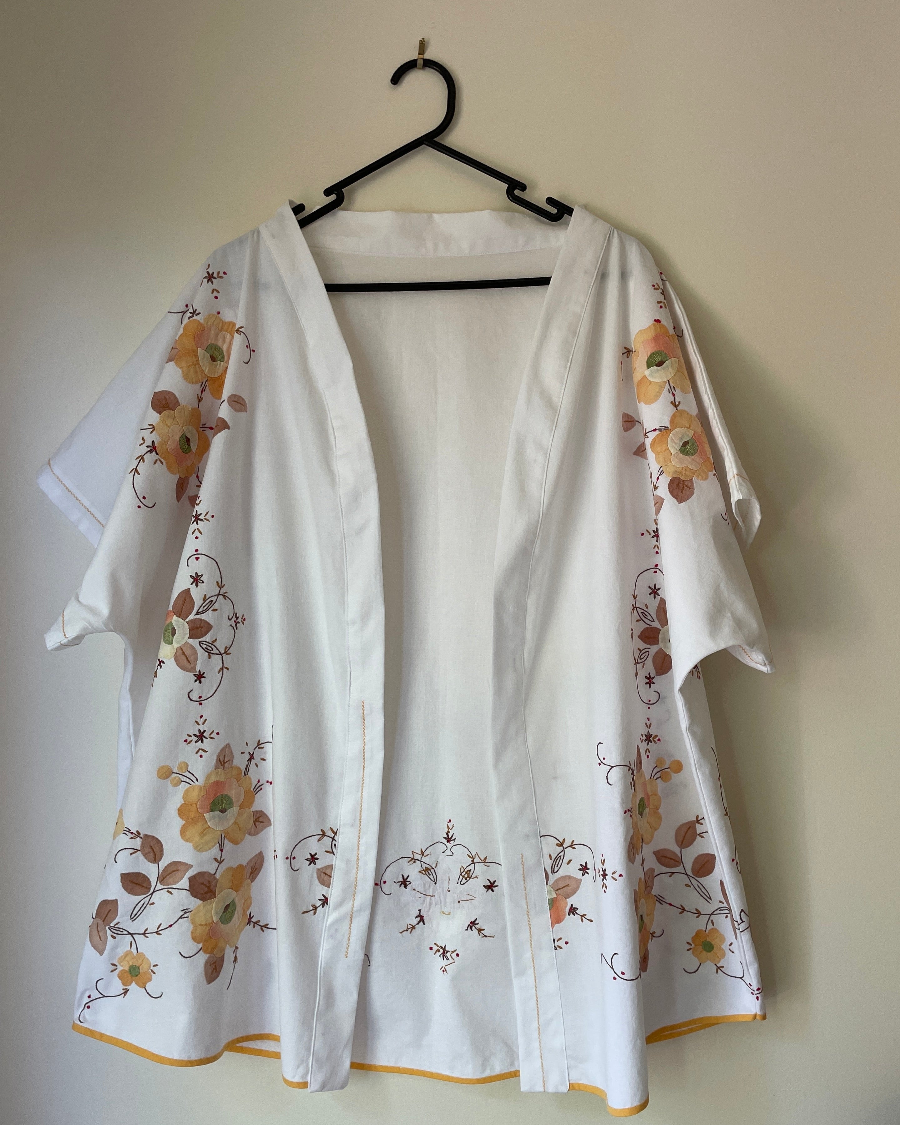 White kimono with floral embroidery on a hanger against a plain wall.