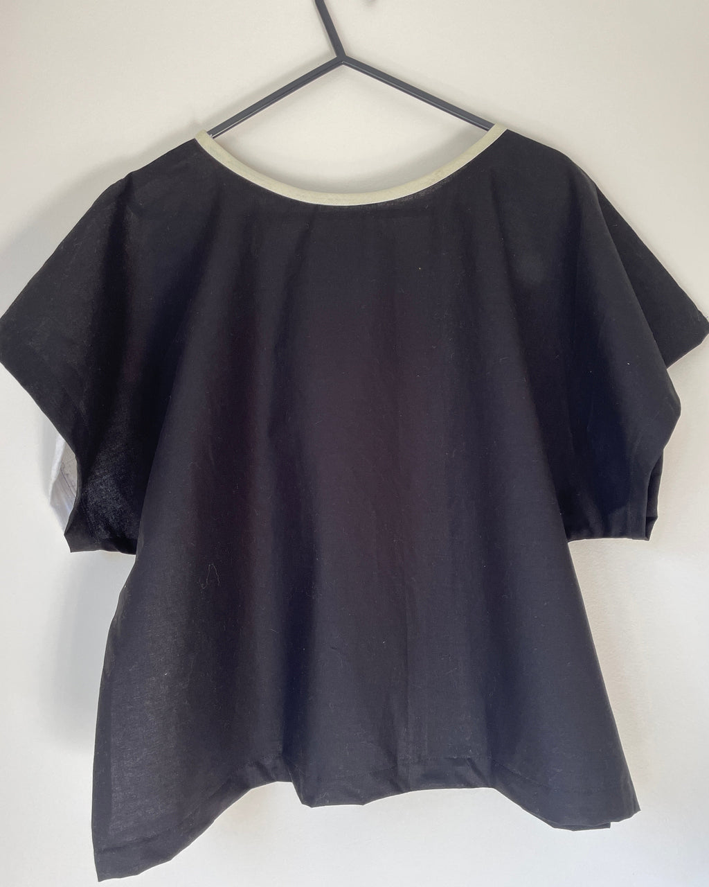 Black boxy top on a hanger against a white background