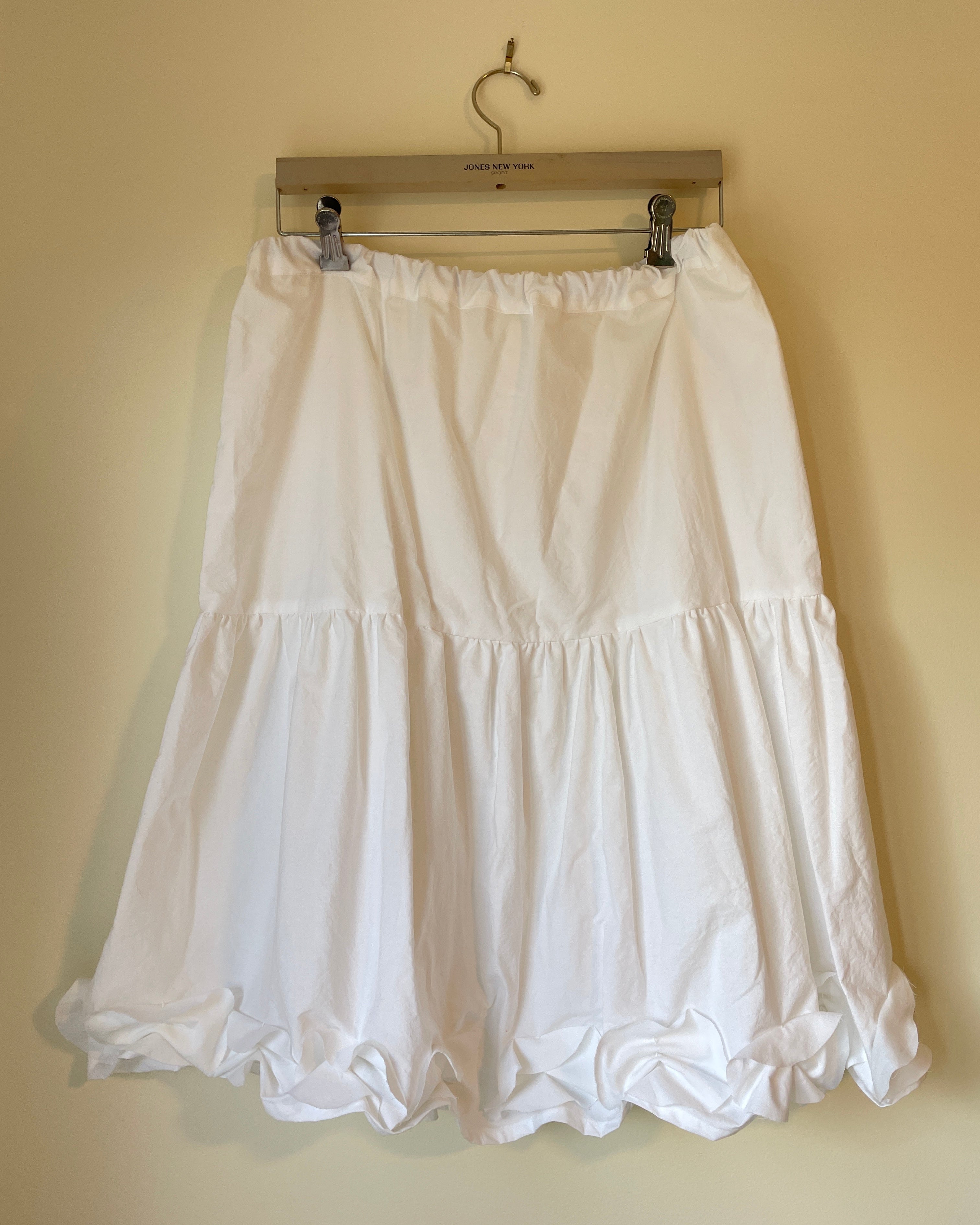 White skirt on a wooden hanger against a beige wall