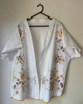 White blouse with floral patterns on a hanger against a plain wall
