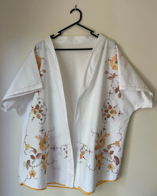 White blouse with floral patterns on a hanger against a plain wall