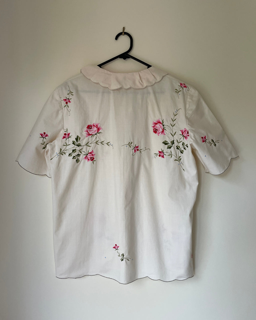 White blouse with floral embroidery on a hanger against a plain wall